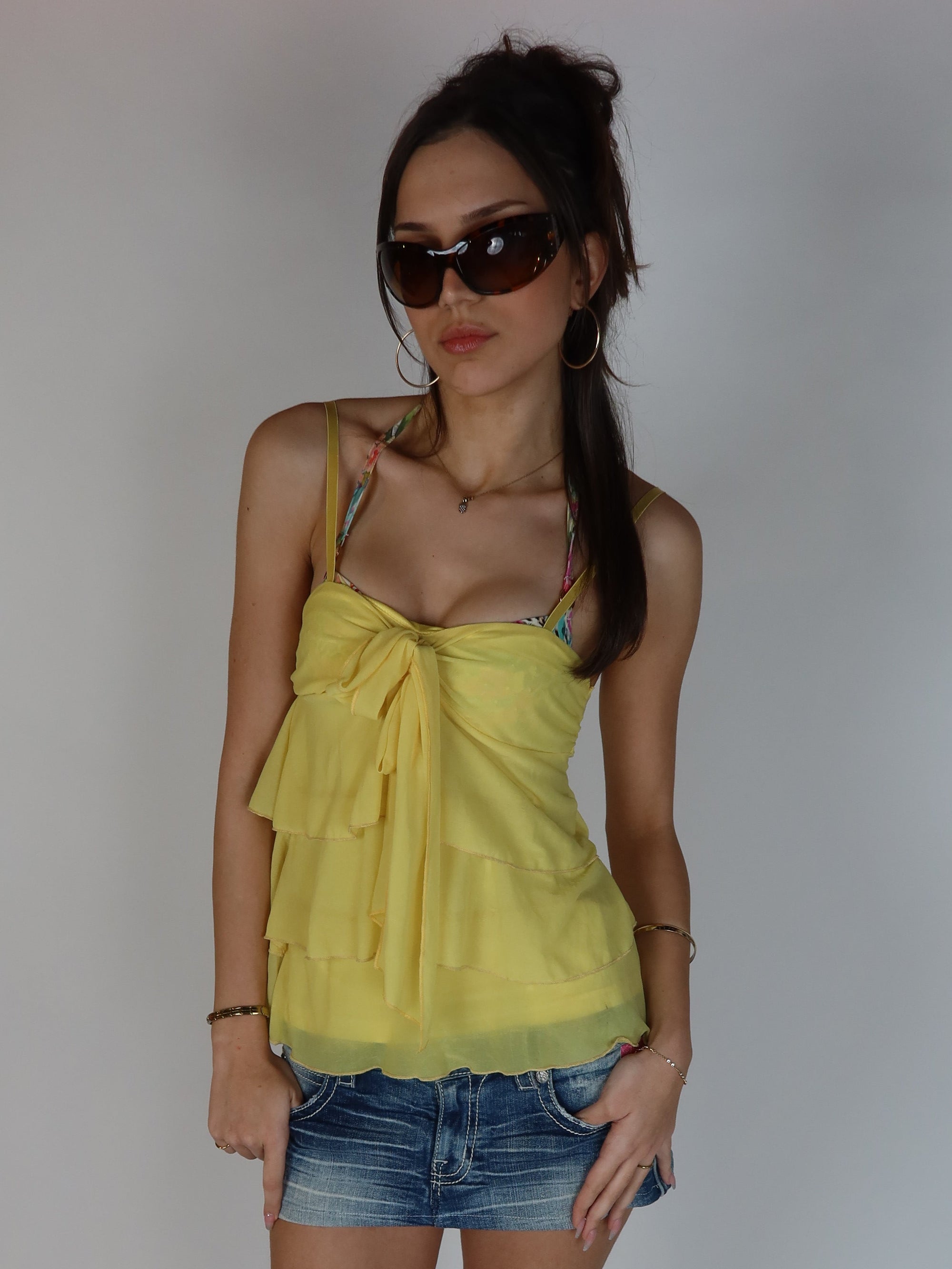 Butter yellow Y2K chiffon cami top with tie-front bust detail, layered ruffle design and spaghetti straps styled with denim shorts