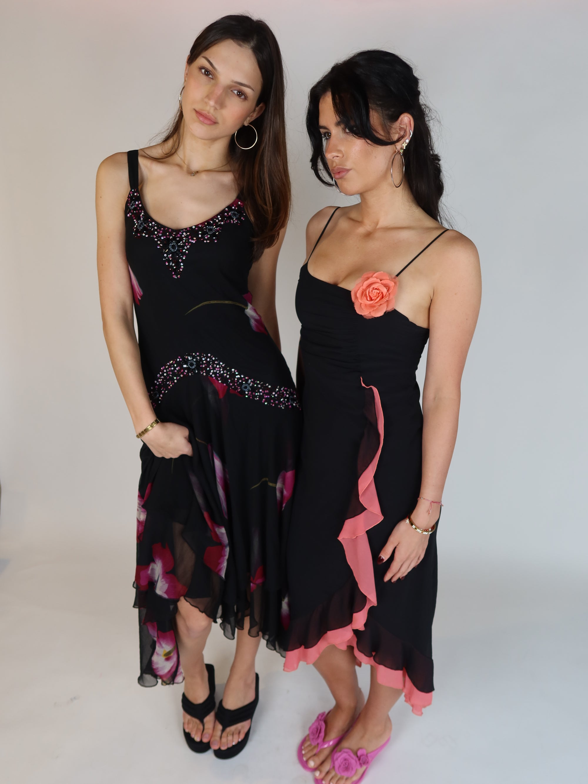 Vintage Y2K black slip dress with pink ruffle trim, floral appliqué detail, spaghetti straps, and asymmetrical midi-length silhouette.