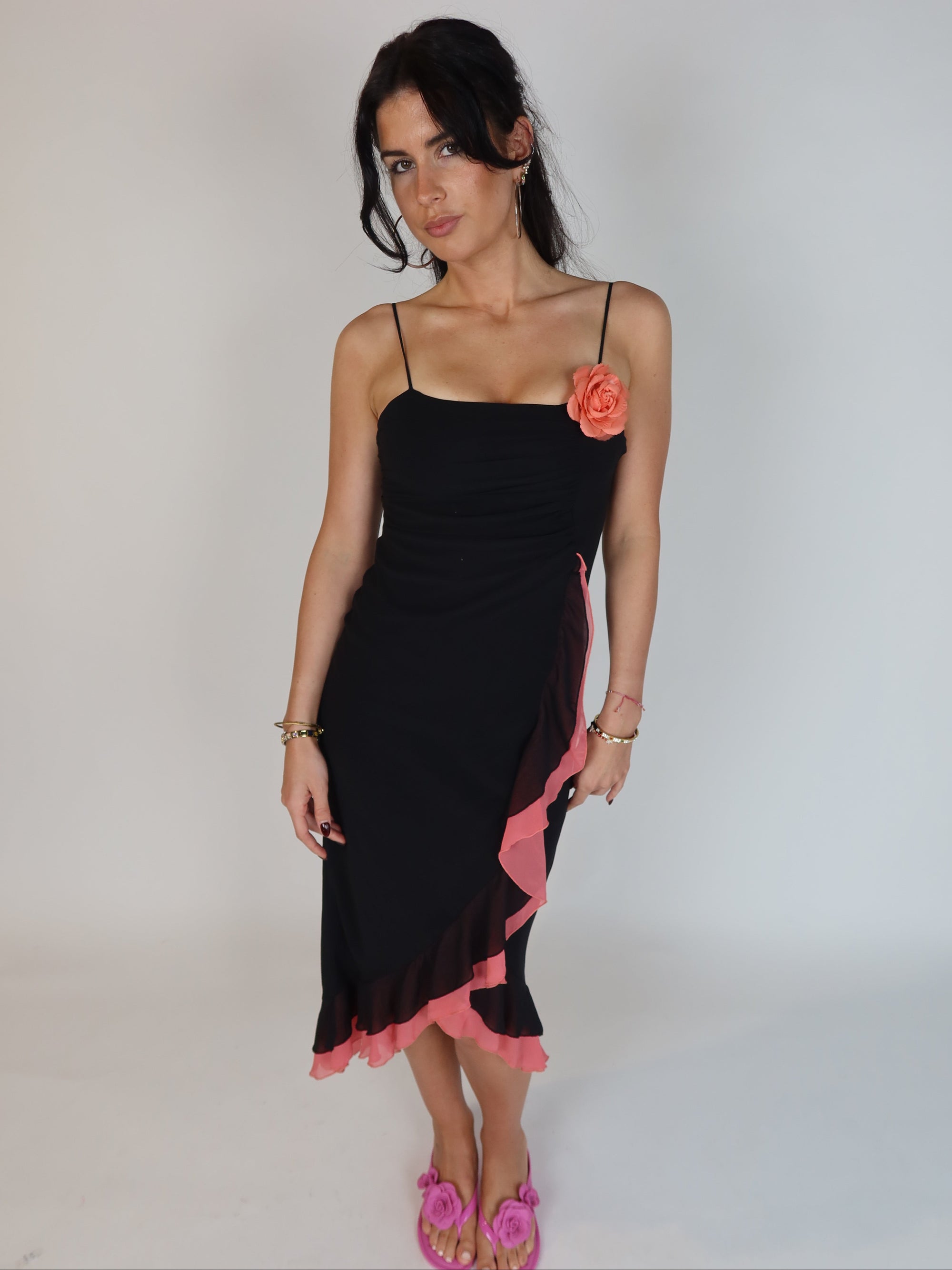 Vintage Y2K black slip dress with pink ruffle trim, floral appliqué detail, spaghetti straps, and asymmetrical midi-length silhouette.