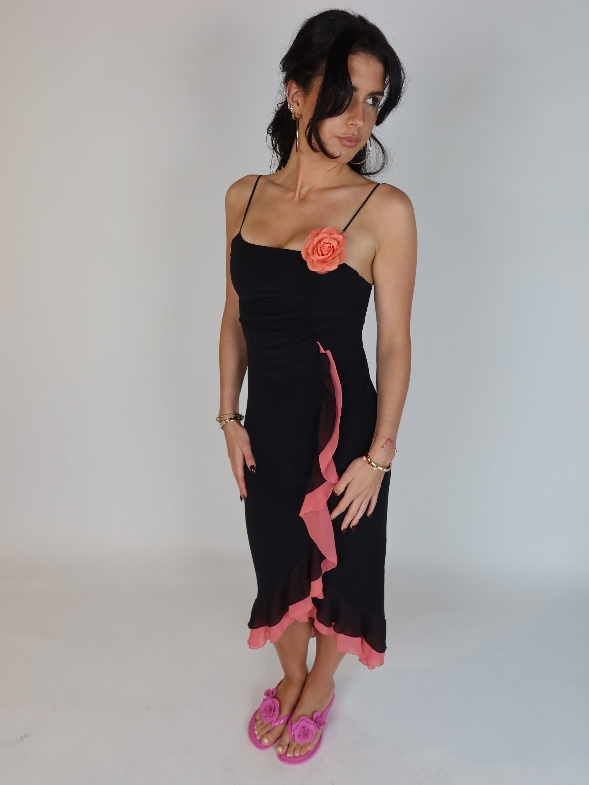 Vintage Y2K black slip dress with pink ruffle trim, floral appliqué detail, spaghetti straps, and asymmetrical midi-length silhouette.