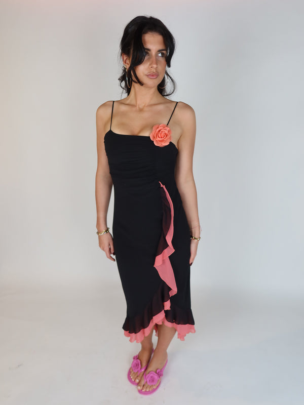 Vintage Y2K black slip dress with pink ruffle trim, floral appliqué detail, spaghetti straps, and asymmetrical midi-length silhouette.