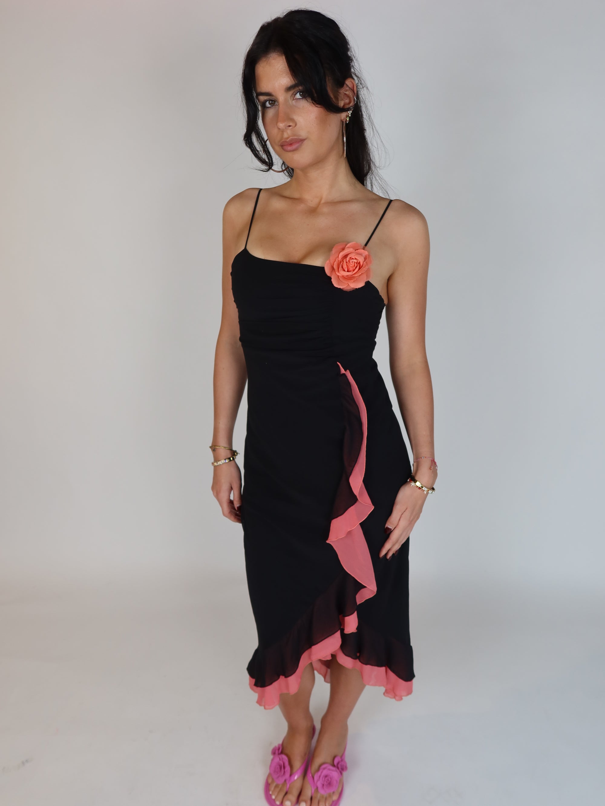 Vintage Y2K black slip dress with pink ruffle trim, floral appliqué detail, spaghetti straps, and asymmetrical midi-length silhouette.