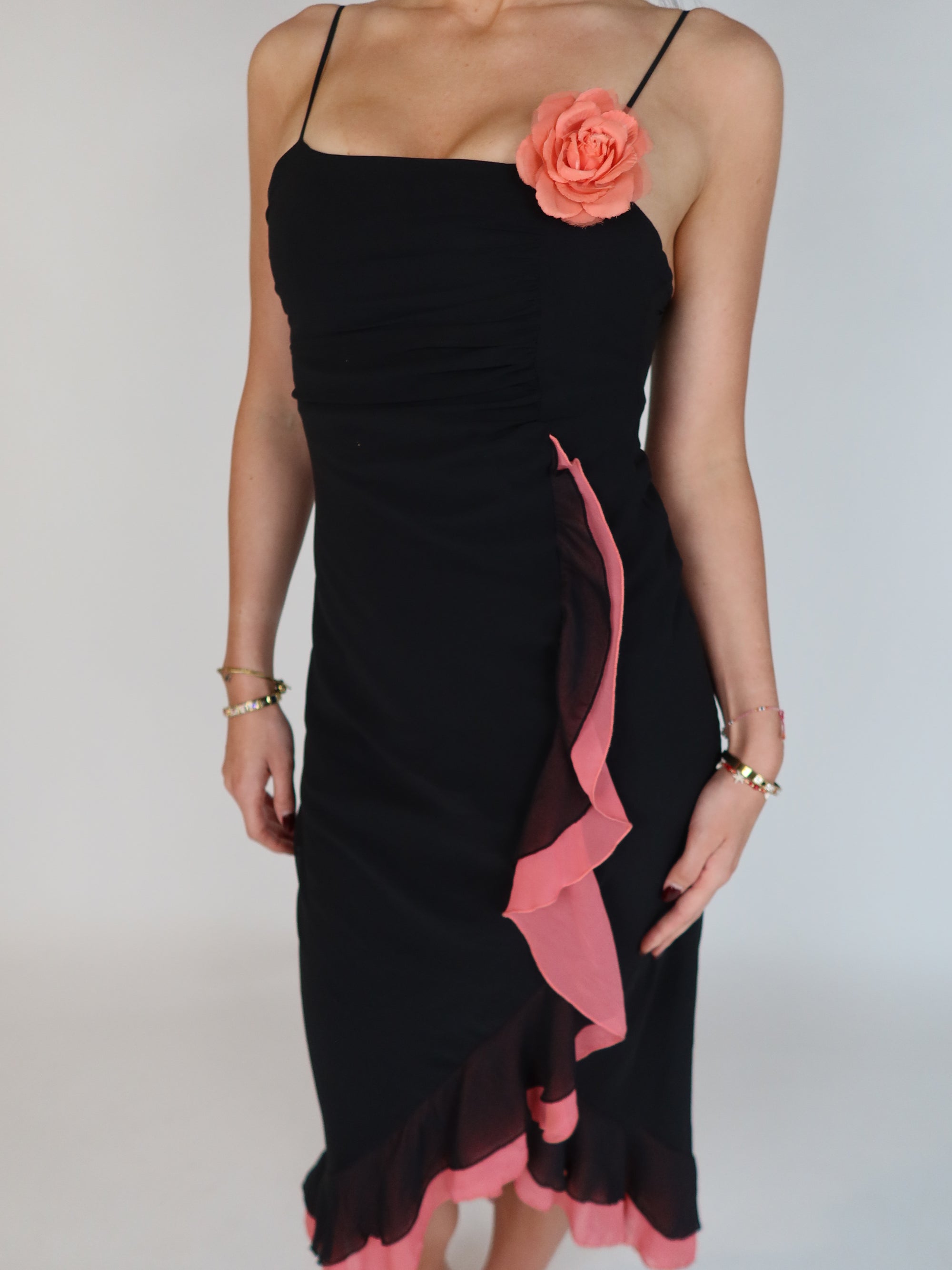 Vintage Y2K black slip dress with pink ruffle trim, floral appliqué detail, spaghetti straps, and asymmetrical midi-length silhouette.