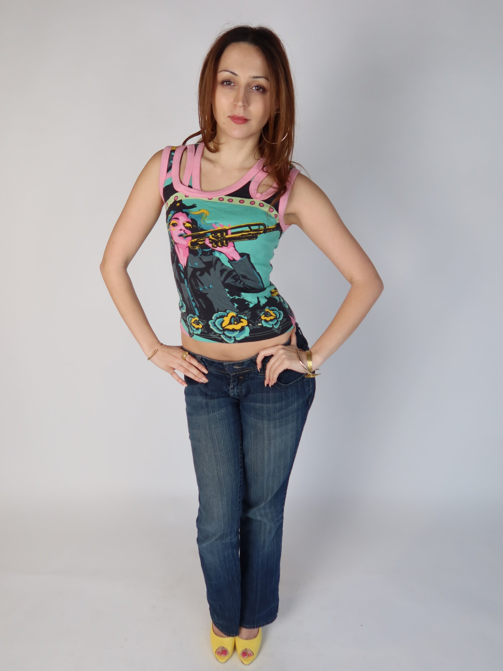 Authentic vintage Y2K teal and pink graphic tank top with a pop art trumpet girl print and pink multi-strap cut out shoulders, shown from front and back views with low-rise jeans.
