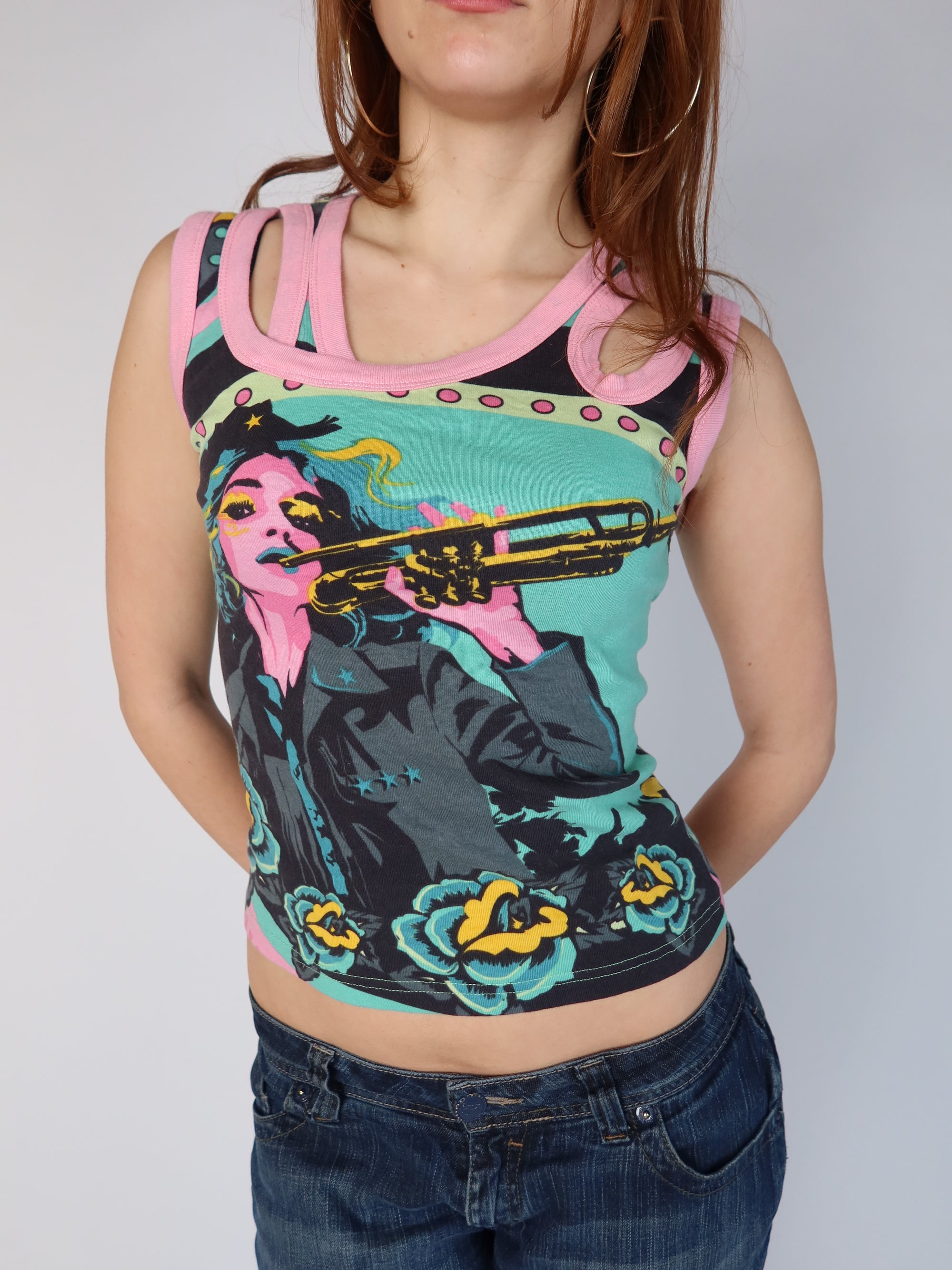 Authentic vintage Y2K teal and pink graphic tank top with a pop art trumpet girl print and pink multi-strap cut out shoulders, shown from front and back views with low-rise jeans.