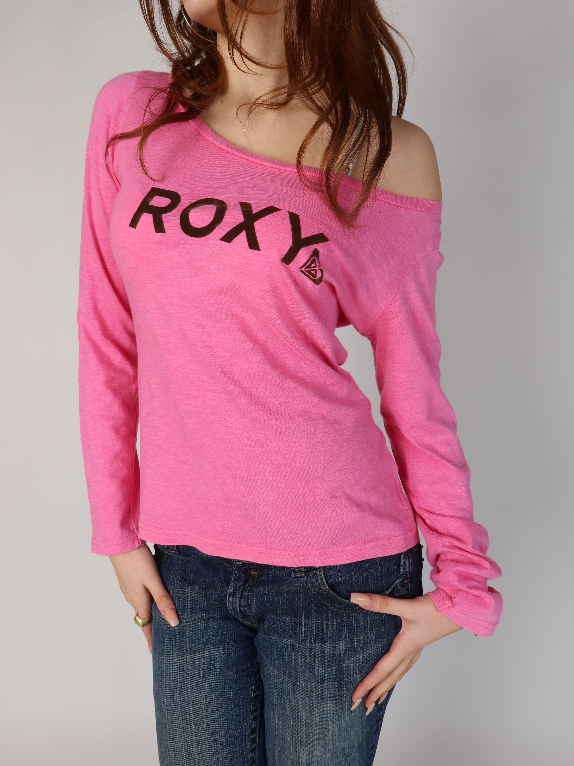 vintage Y2K Roxy bubblegum pink long sleeve top with an off-shoulder neckline, brown flocked logo text on front and back, shown from front and back views with low-rise jeans.