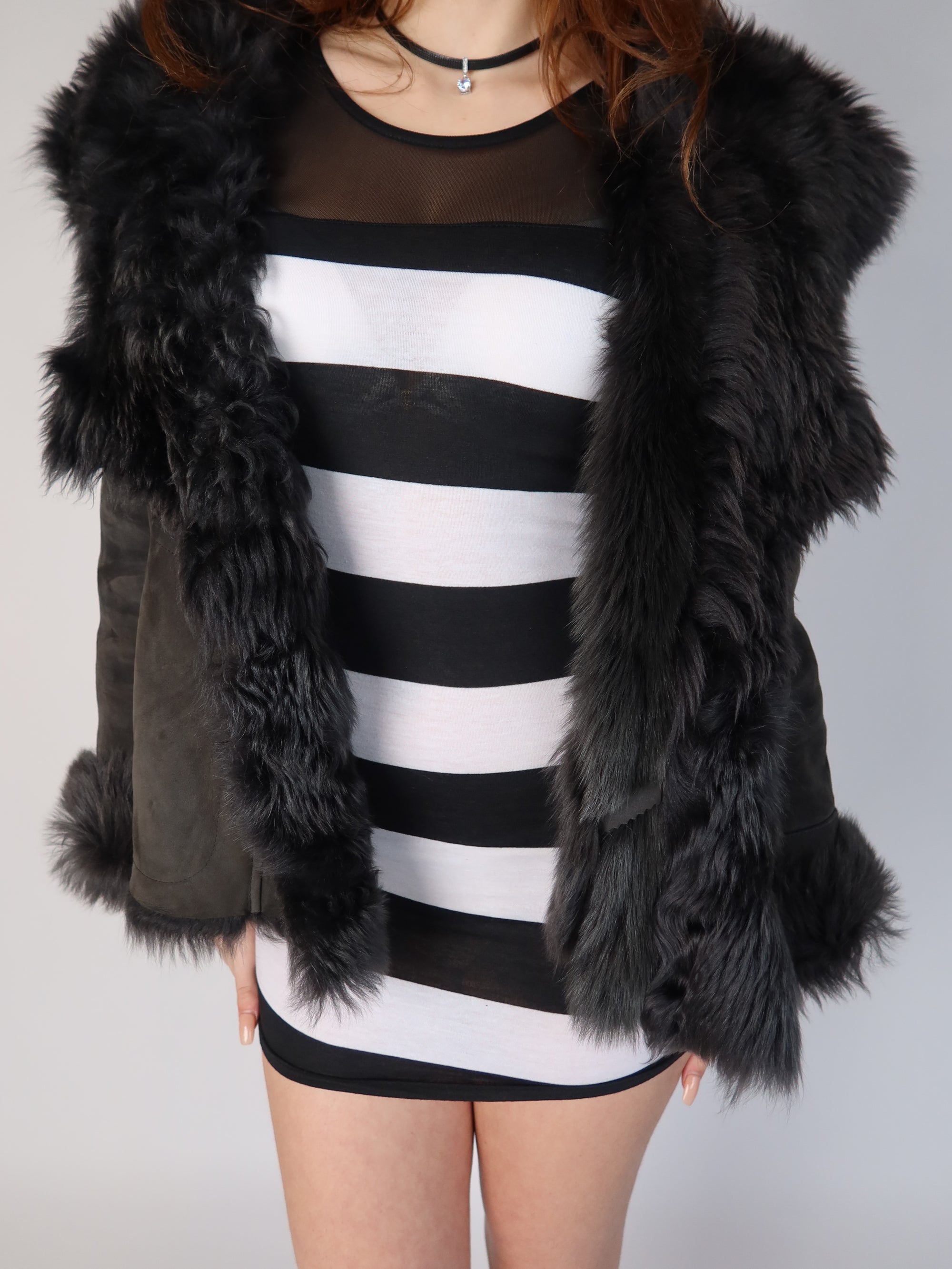 Authentic vintage Y2K premium black Italian shearling lambskin jacket featuring a completely fluffy fur-lined interior, an oversized shaggy fur collar, trim, and matching fur-cuffed sleeves, shown from front and back views with a striped mini dress.